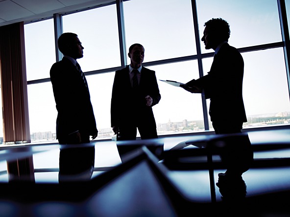 Three silhouetted businessmen talk in an office 